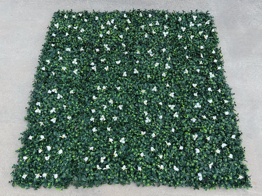 Multiple dense green artificial greenery wall panels connected to form a seamless faux green wall with white floral accents
