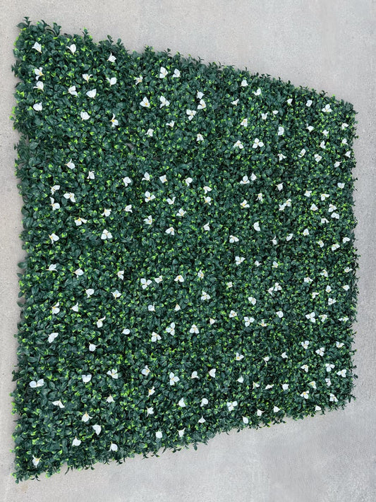 Multiple dense green artificial greenery wall panels connected to form a seamless faux green wall with white floral accents