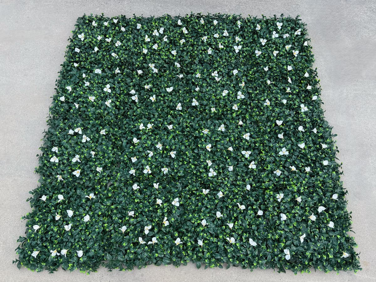 Multiple dense green artificial greenery wall panels connected to form a seamless faux green wall with white floral accents