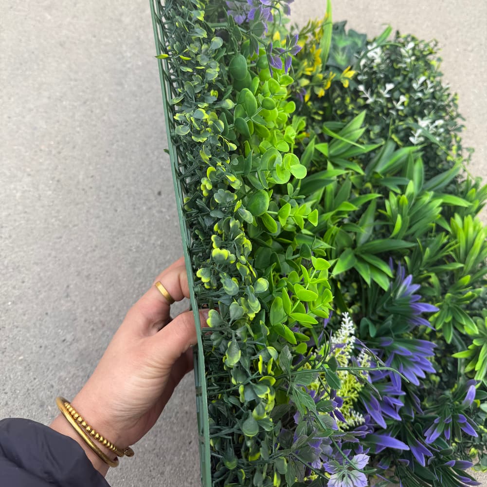 Close-up of mixed greenery wall panel showing layered faux leaves and floral accents with high-density coverage