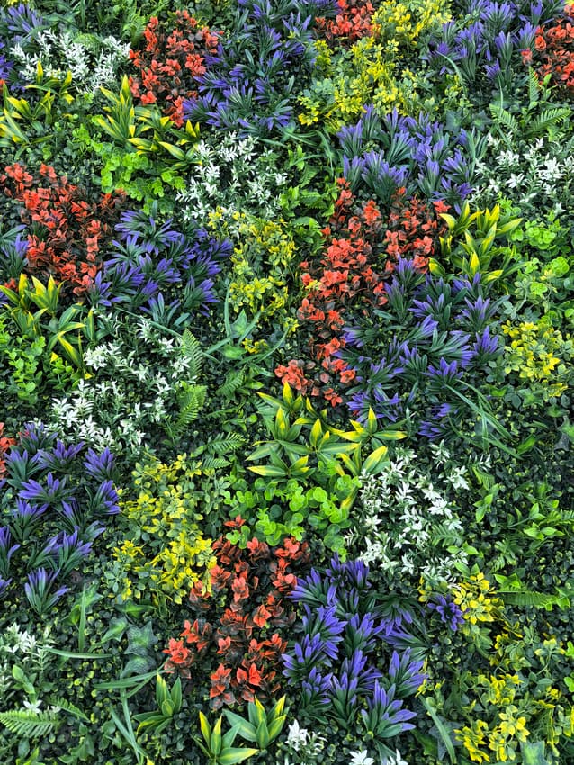 Detail view of artificial greenery wall panel showing purple, yellow, orange, and green leaf variations without floral elements